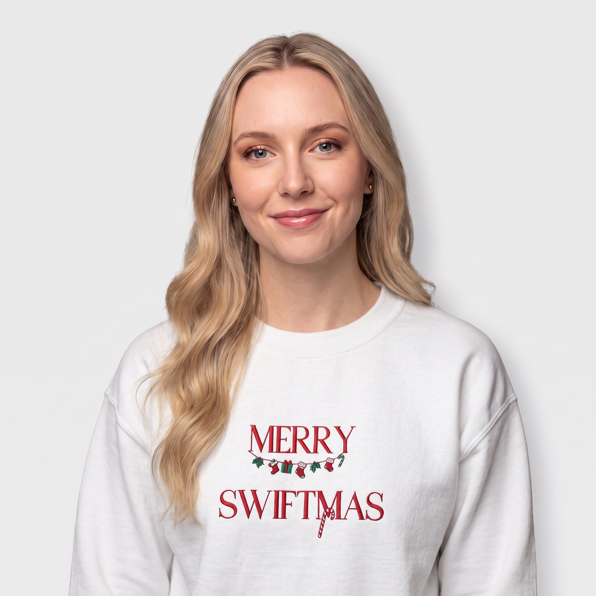 Model wearing a white sweatshirt with "Merry Swiftmas" embroidered text with a stocking garland and candy cane, holiday Taylor Swift design