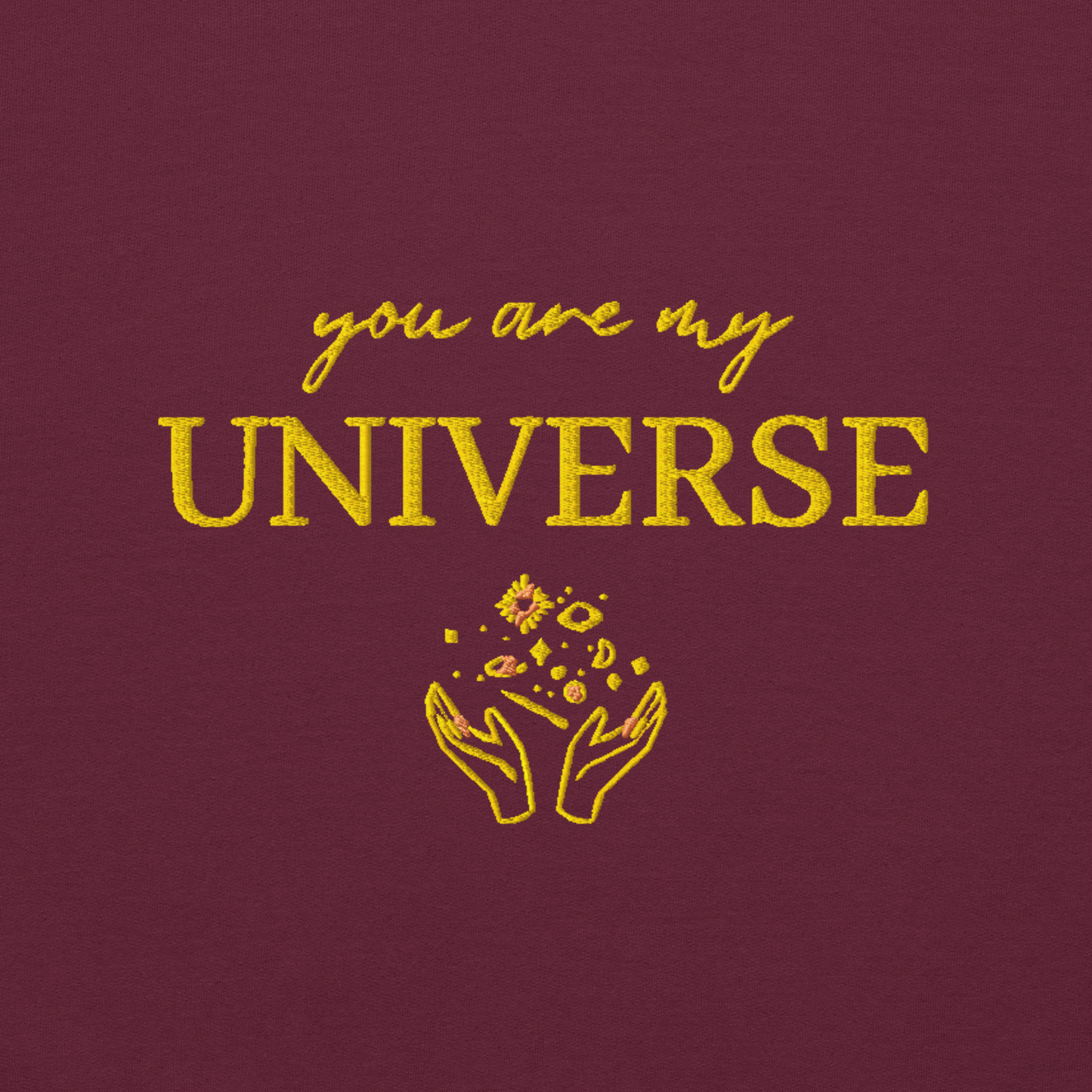 Maroon crewneck sweatshirt featuring yellow typography that reads “you are my Universe” with minimalist hands holding stars illustration -inspired by Coldplay’s hit song “My Universe”, aesthetic fan apparel for music lovers.