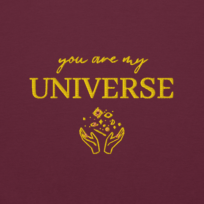 Maroon crewneck sweatshirt featuring yellow typography that reads “you are my Universe” with minimalist hands holding stars illustration -inspired by Coldplay’s hit song “My Universe”, aesthetic fan apparel for music lovers.