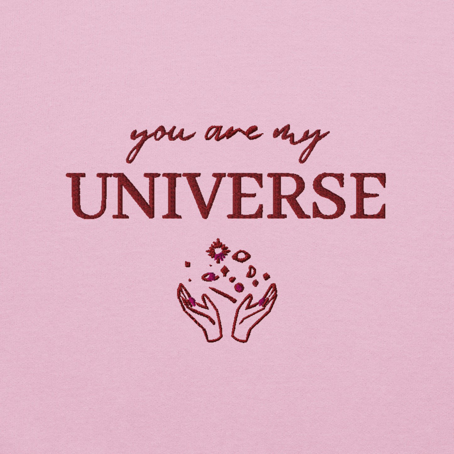 Pink crewneck sweatshirt featuring maroon typography that reads “you are my Universe” with minimalist hands holding stars illustration -inspired by Coldplay’s hit song “My Universe”, aesthetic fan apparel for music lovers.