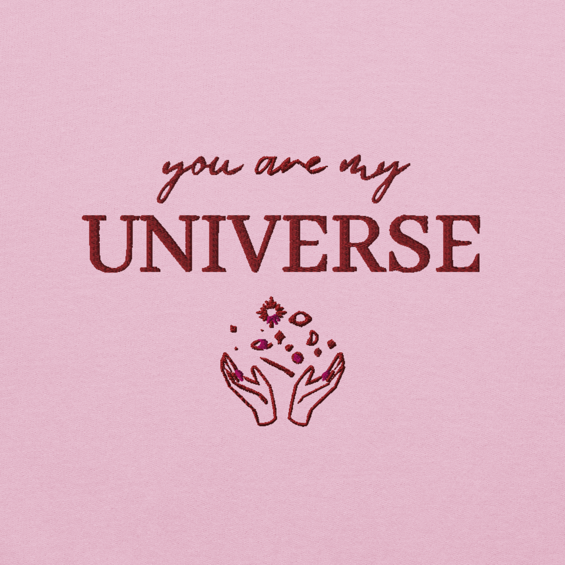 Pink crewneck sweatshirt featuring maroon typography that reads “you are my Universe” with minimalist hands holding stars illustration -inspired by Coldplay’s hit song “My Universe”, aesthetic fan apparel for music lovers.