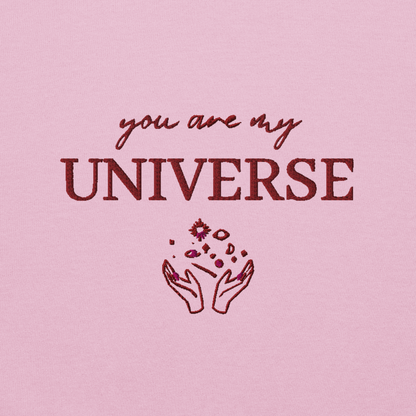 Pink crewneck sweatshirt featuring maroon typography that reads “you are my Universe” with minimalist hands holding stars illustration -inspired by Coldplay’s hit song “My Universe”, aesthetic fan apparel for music lovers.