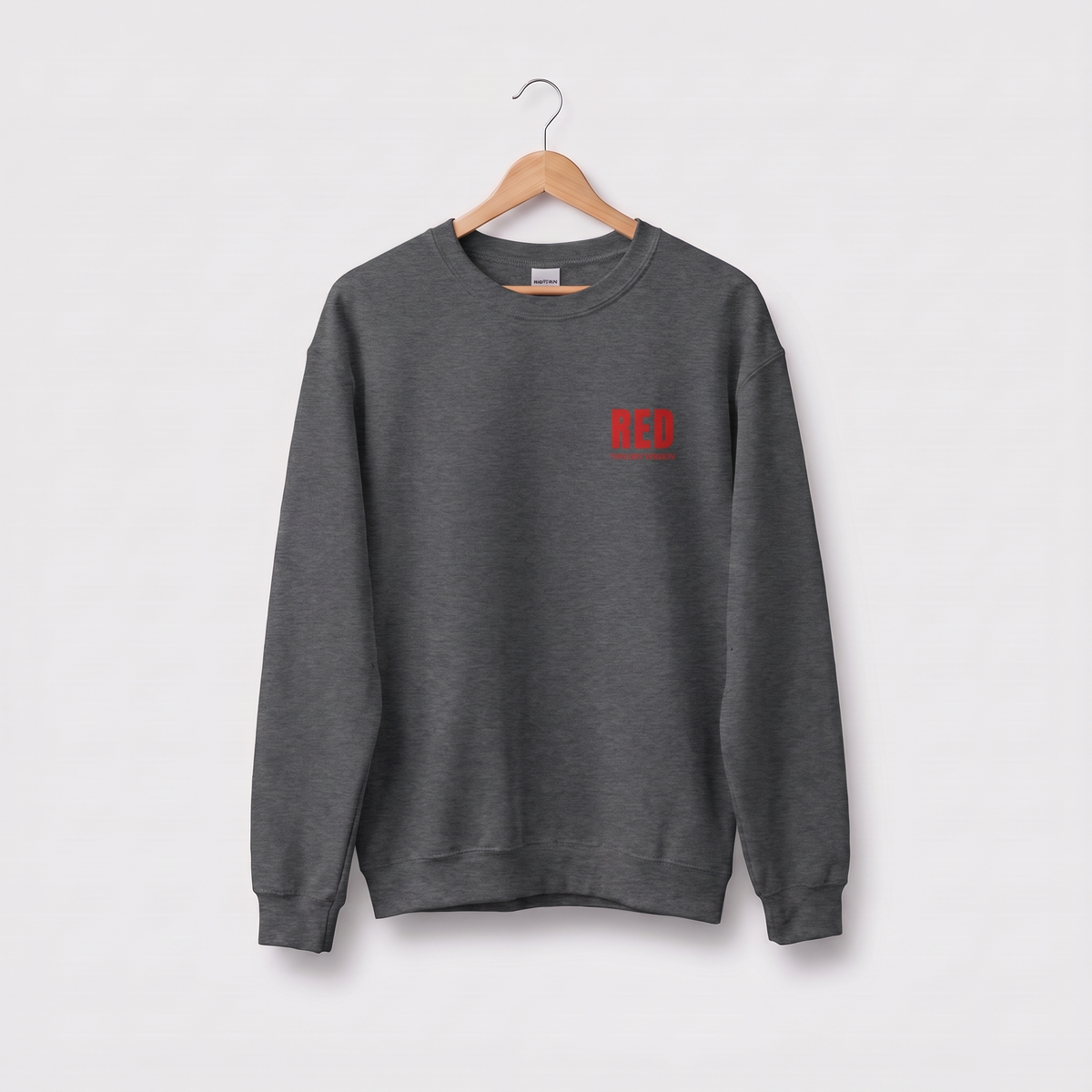 A dark gray crewneck sweatshirt hanging on a wooden hanger against a light gray background, featuring a small red embroidered 'RED' logo on the left chest, with 'Taylor's version' underneath.