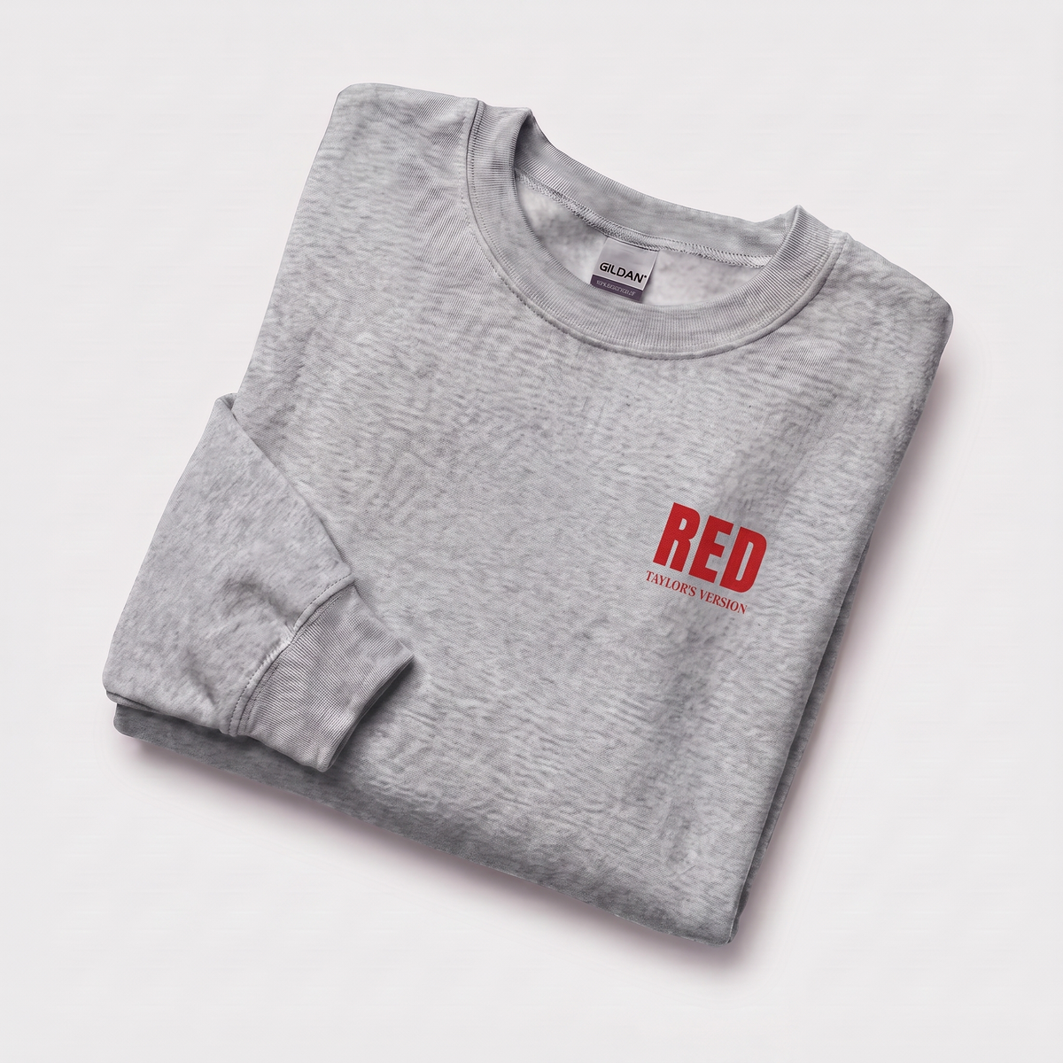 A folded light gray heather crewneck sweatshirt with 'RED' and 'TAYLOR'S VERSION' printed in red on the chest, displayed on a clean white background.