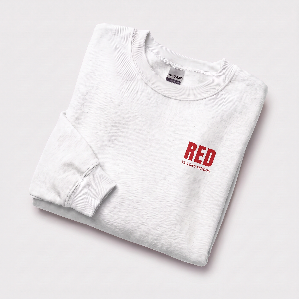 A folded white crewneck sweatshirt with a red graphic on the left chest reading 'RED TAYLOR'S VERSION', displayed on a clean white background.