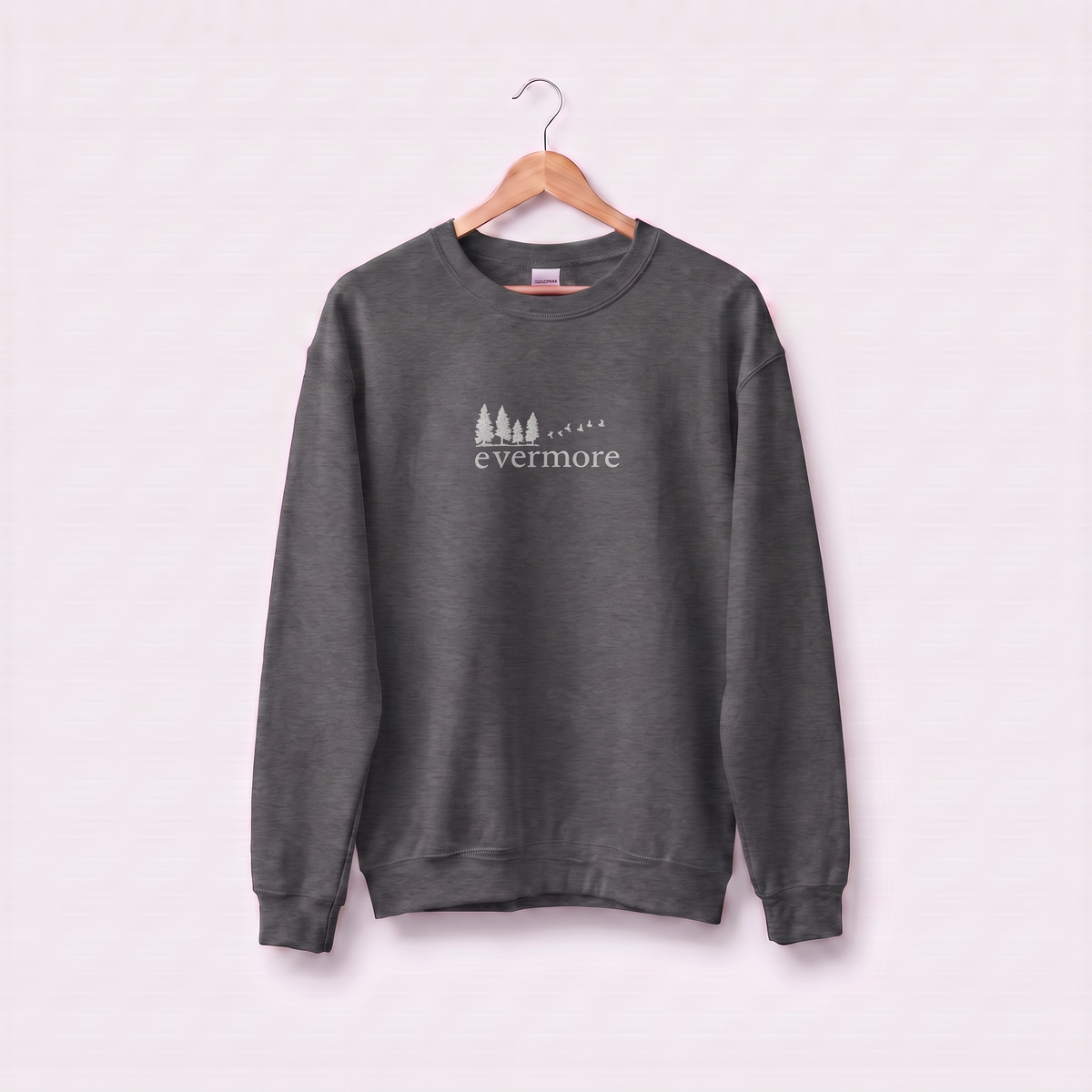 Dark heather Evermore sweatshirt inspired by Taylor Swift's evermore album, embroidered pine tree and flying birds logo, cottagecore Swiftie merch on a wooden hanger