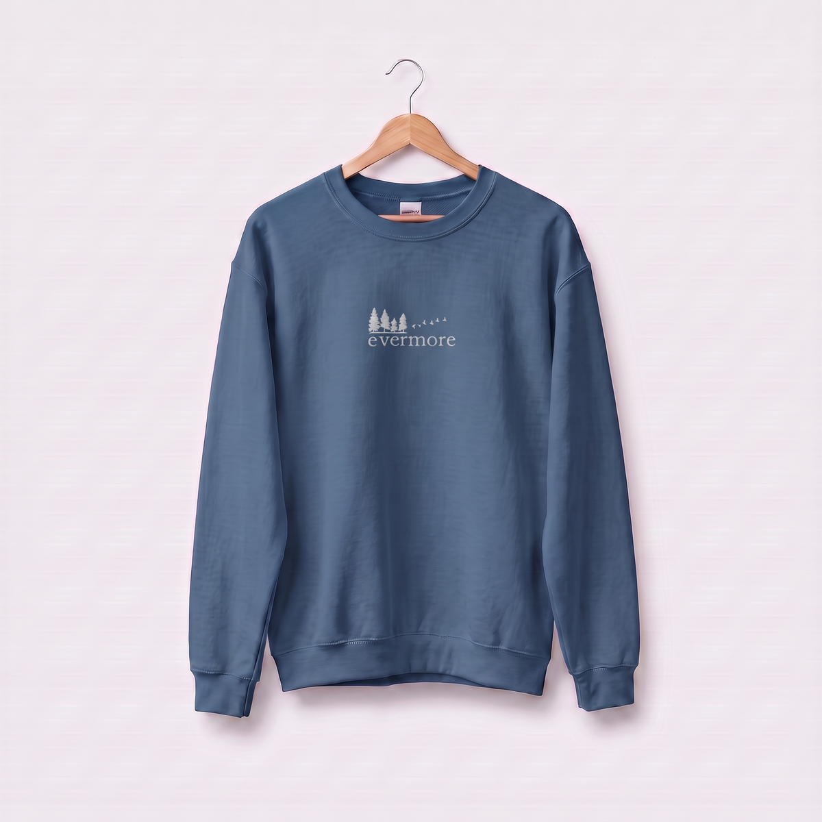 Indigo Blue Evermore sweatshirt inspired by Taylor Swift's evermore album, embroidered pine tree and flying birds logo, cottagecore Swiftie merch on a wooden hanger