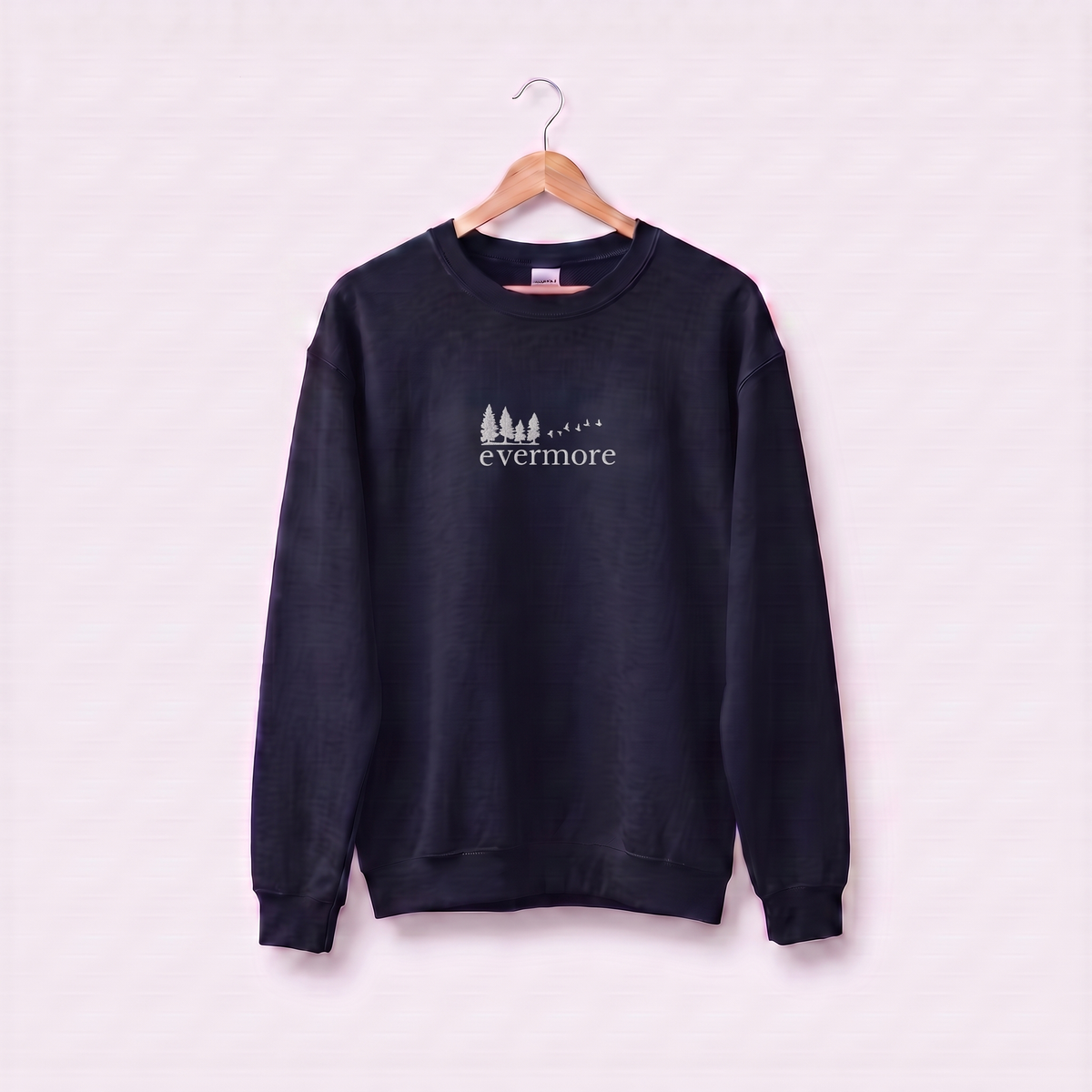 Navy Evermore sweatshirt inspired by Taylor Swift's evermore album, embroidered pine tree and flying birds logo, cottagecore Swiftie merch on a wooden hanger