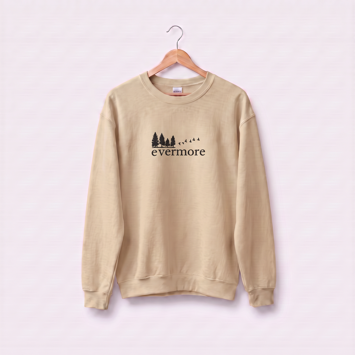 Sand Evermore sweatshirt inspired by Taylor Swift's evermore album, embroidered pine tree and flying birds logo, cottagecore Swiftie merch on a wooden hanger