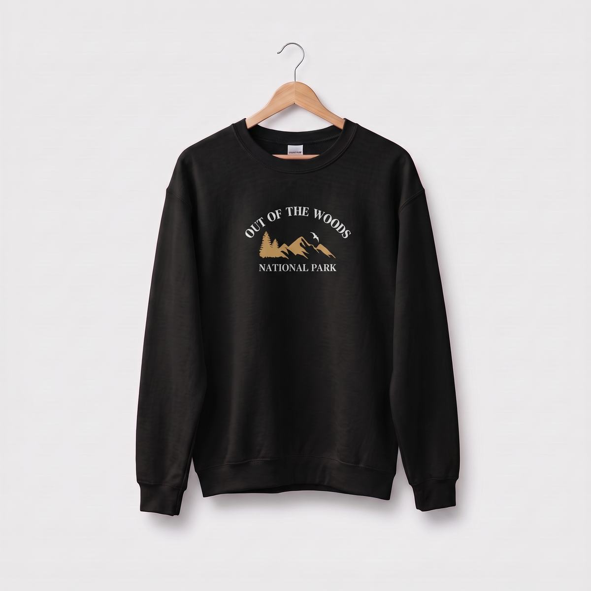 A black crewneck sweatshirt hanging on a wooden hanger against a light gray background. The sweatshirt features a graphic print on the chest reading 'OUT OF THE WOODS NATIONAL PARK' in white text above a brown mountain illustration.
