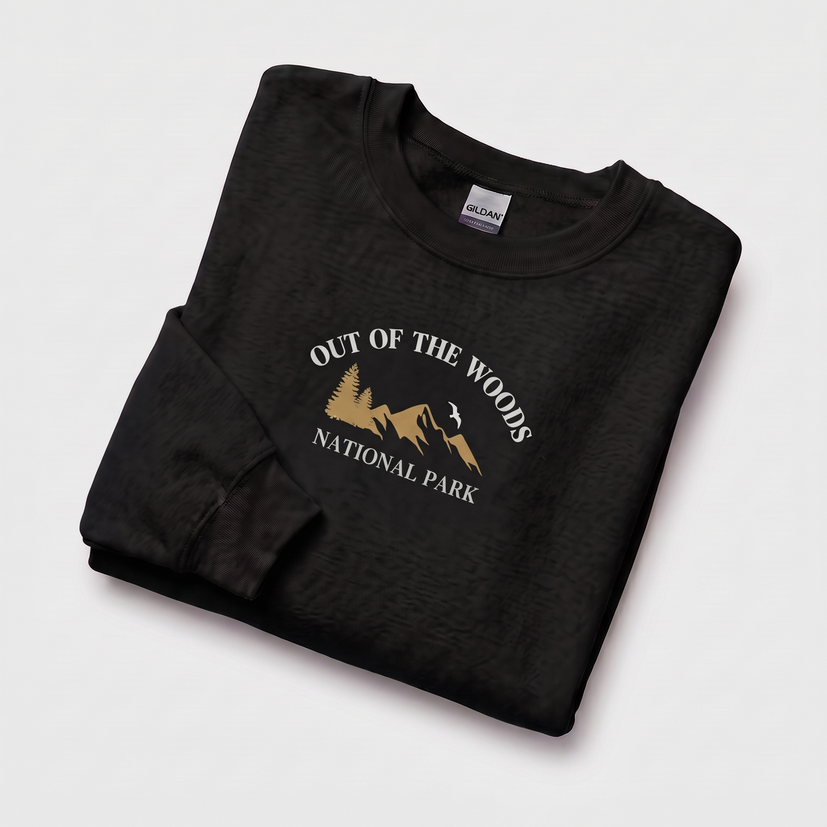 A folded black sweatshirt with a 'OUT OF THE WOODS NATIONAL PARK' graphic in gold and white, displayed on a light gray background.
