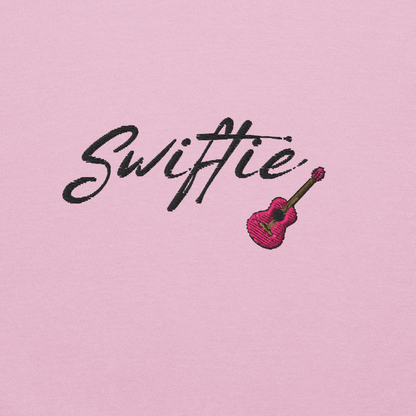 Pink crewneck sweatshirt with black “Swiftie” script and small guitar graphic on the chest, Taylor Swift inspired fan merch, cozy unisex pullover for concerts and everyday wear