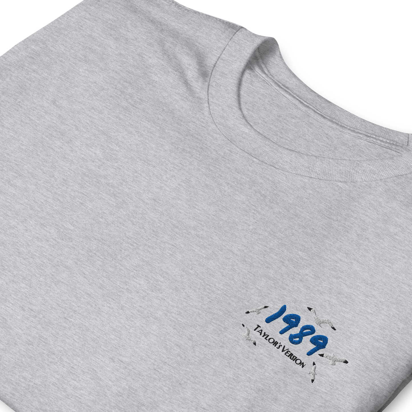 Grey Taylor Swift 1989 (Taylor’s Version) t-shirt featuring a minimalist chest print with blue “1989” lettering and seagull details. Soft unisex tee inspired by Taylor Swift’s 1989 album, perfect for Swifties, concert outfits, and casual pop music streetwear looks