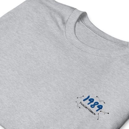 Grey Taylor Swift 1989 (Taylor’s Version) t-shirt featuring a minimalist chest print with blue “1989” lettering and seagull details. Soft unisex tee inspired by Taylor Swift’s 1989 album, perfect for Swifties, concert outfits, and casual pop music streetwear looks
